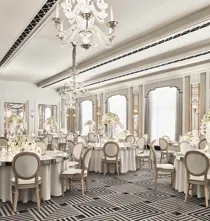 The Ballroom at Claridge’s set for an elegant event with round tables draped in white linens, floral centrepieces of white blooms, crystal chandeliers, and mirrored Art Deco details.