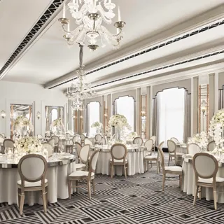 The Ballroom at Claridge’s set for an elegant event with round tables draped in white linens, floral centrepieces of white blooms, crystal chandeliers, and mirrored Art Deco details.