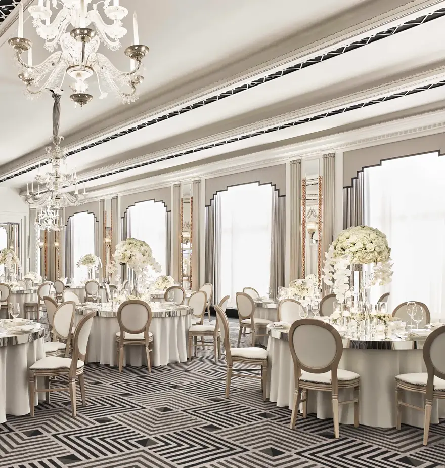 The Ballroom at Claridge’s set for an elegant event with round tables draped in white linens, floral centrepieces of white blooms, crystal chandeliers, and mirrored Art Deco details.