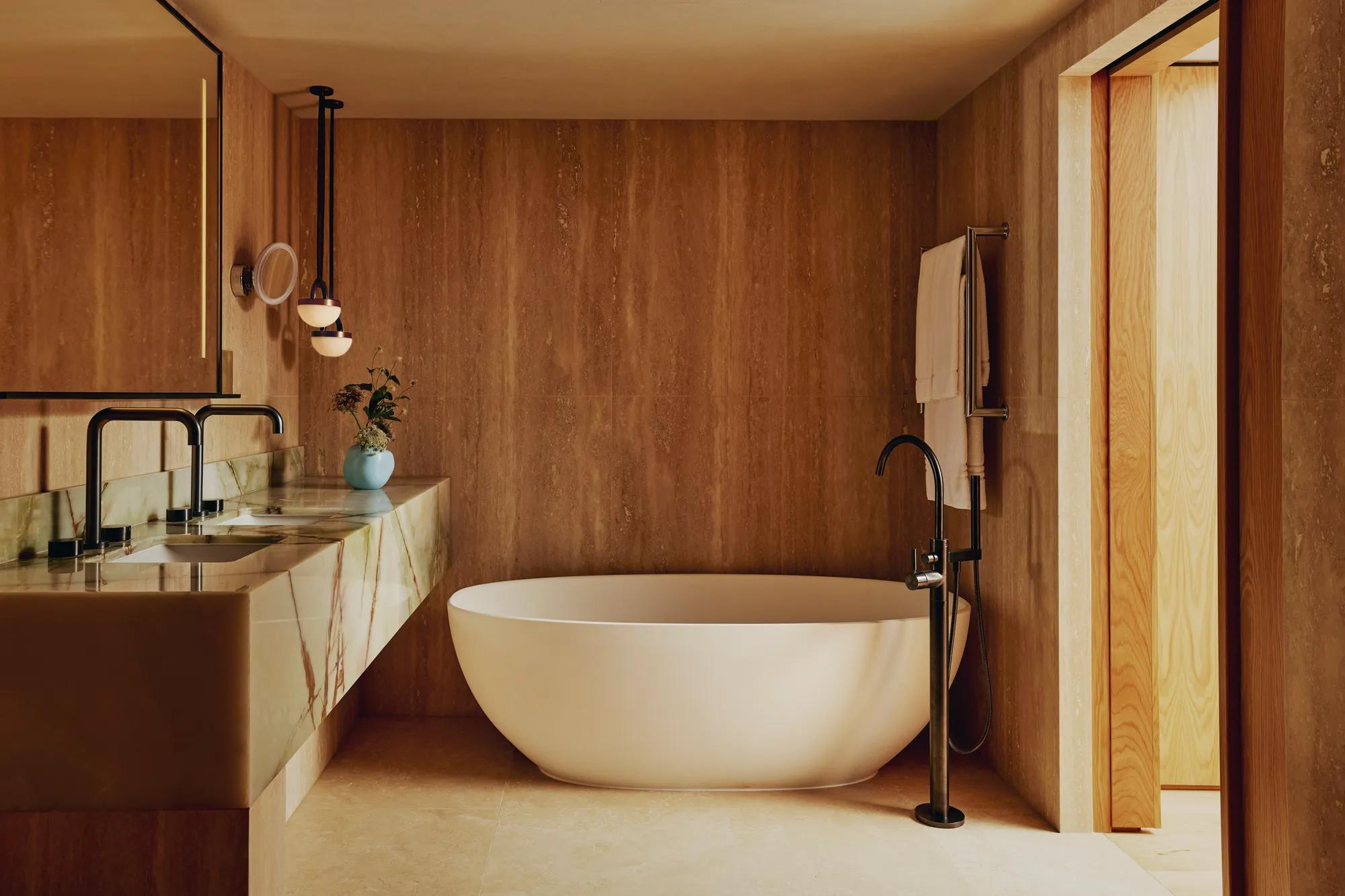 Luxury bathroom with a freestanding oval bathtub, marble double sink, and warm wood-panelled walls.