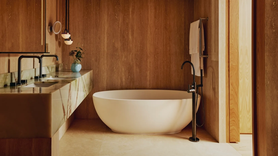 Luxury bathroom with a freestanding oval bathtub, marble double sink, and warm wood-panelled walls.
