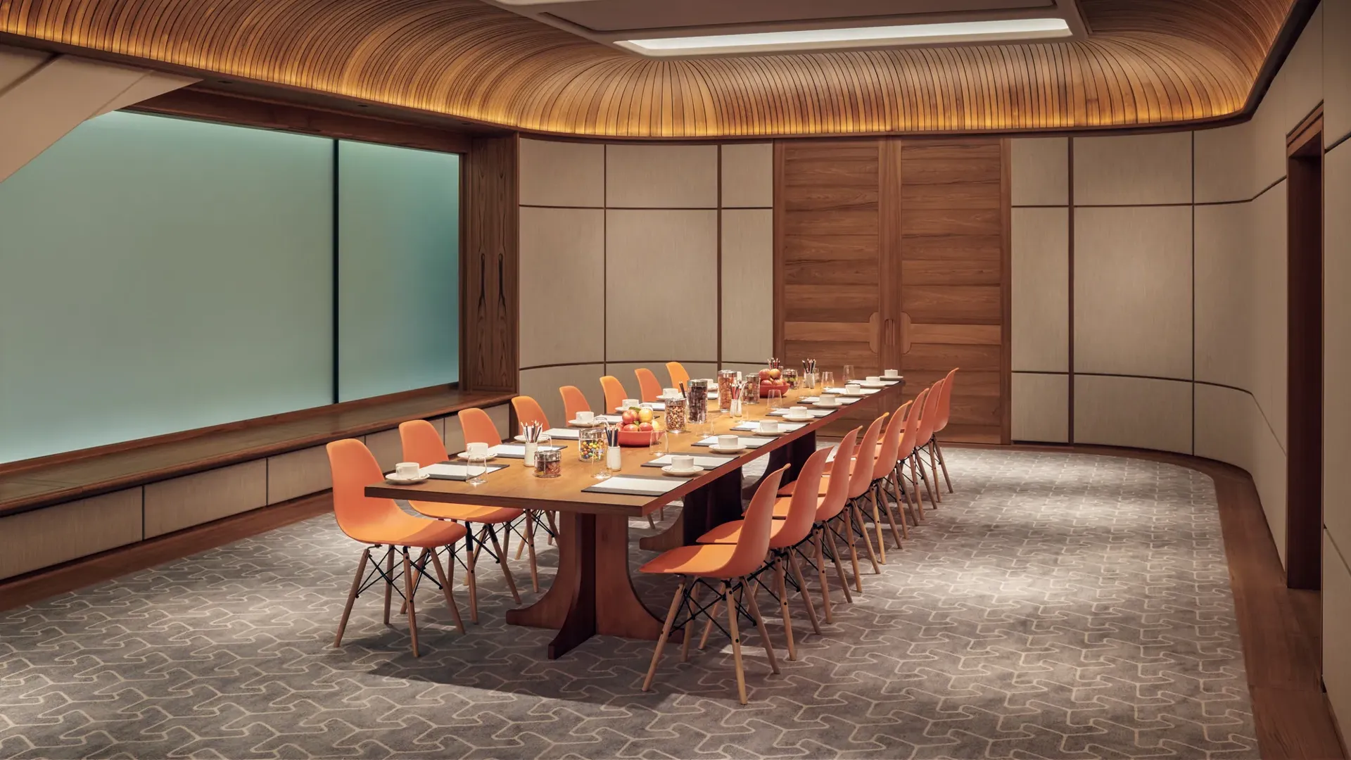 Modern meeting room with long wooden table, orange chairs, and wood-panelled ceiling set for a business event.