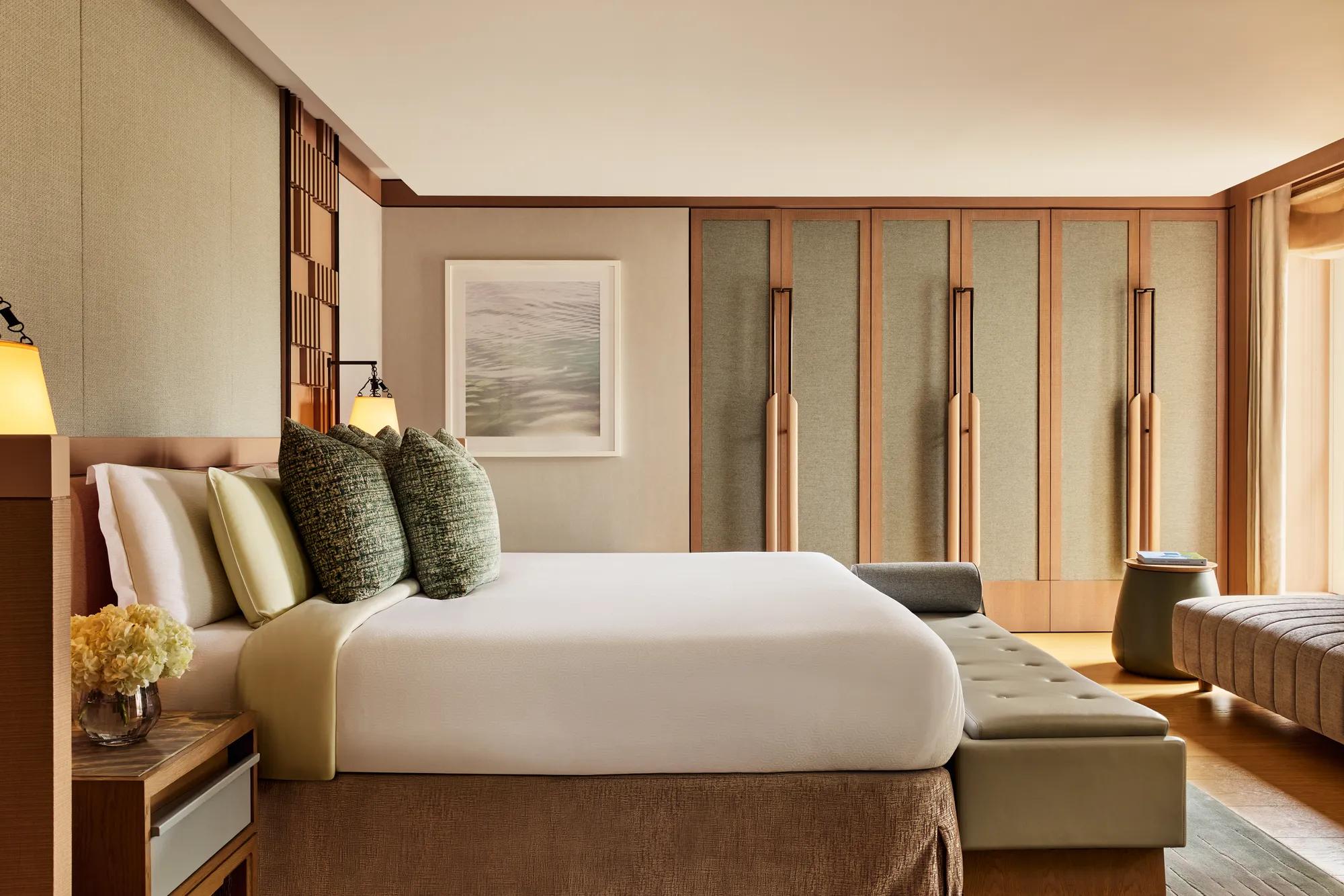 Spacious bedroom with king bed, textured cushions, bench seating, and built-in wardrobes in warm neutral tones