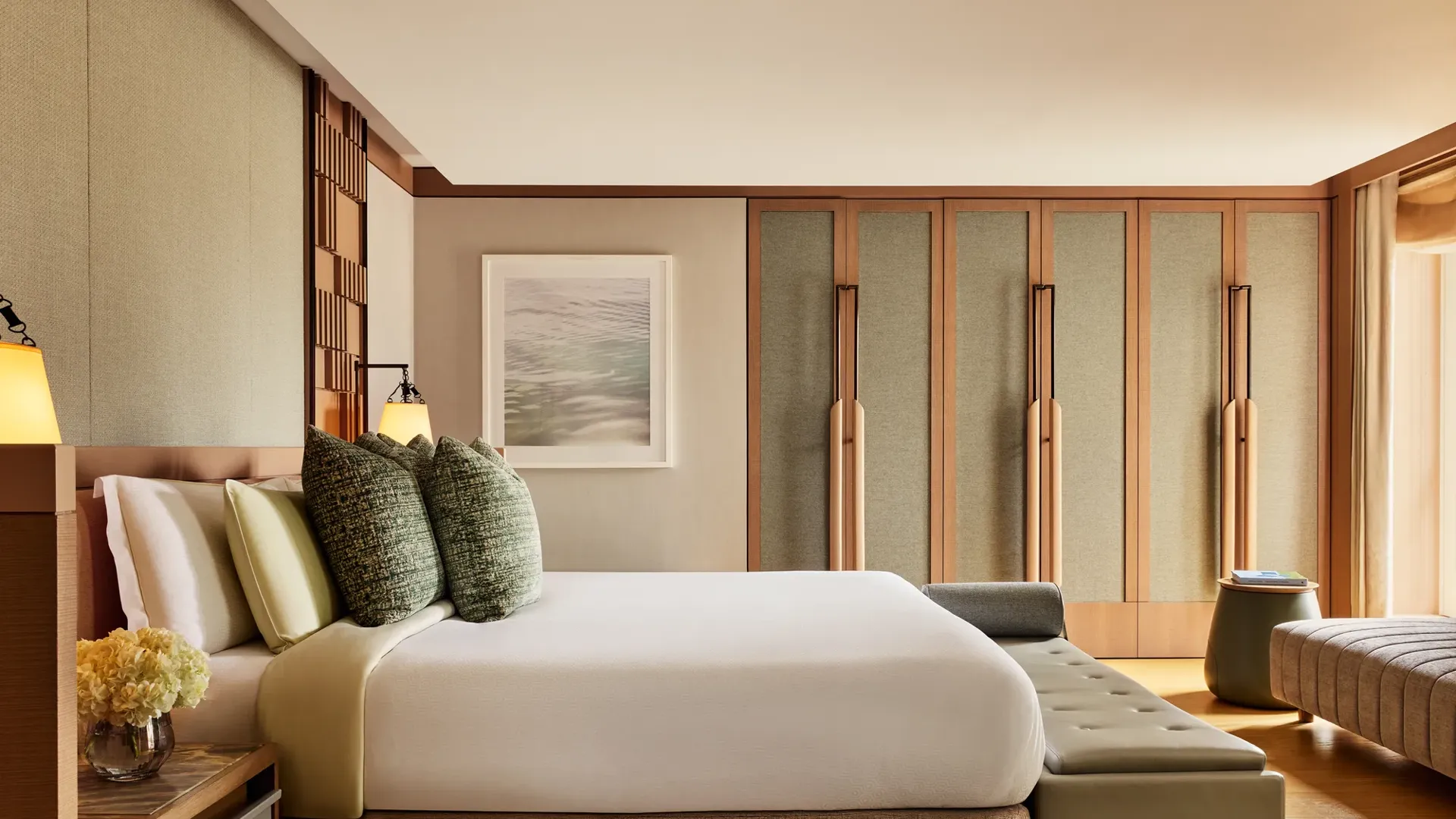 Spacious bedroom with king bed, textured cushions, bench seating, and built-in wardrobes in warm neutral tones