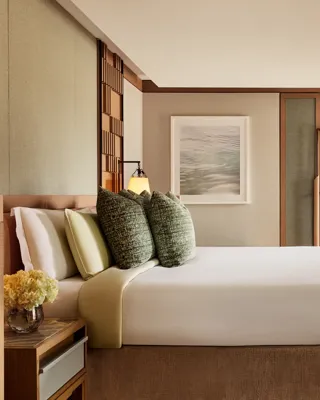 Spacious bedroom with king bed, textured cushions, bench seating, and built-in wardrobes in warm neutral tones