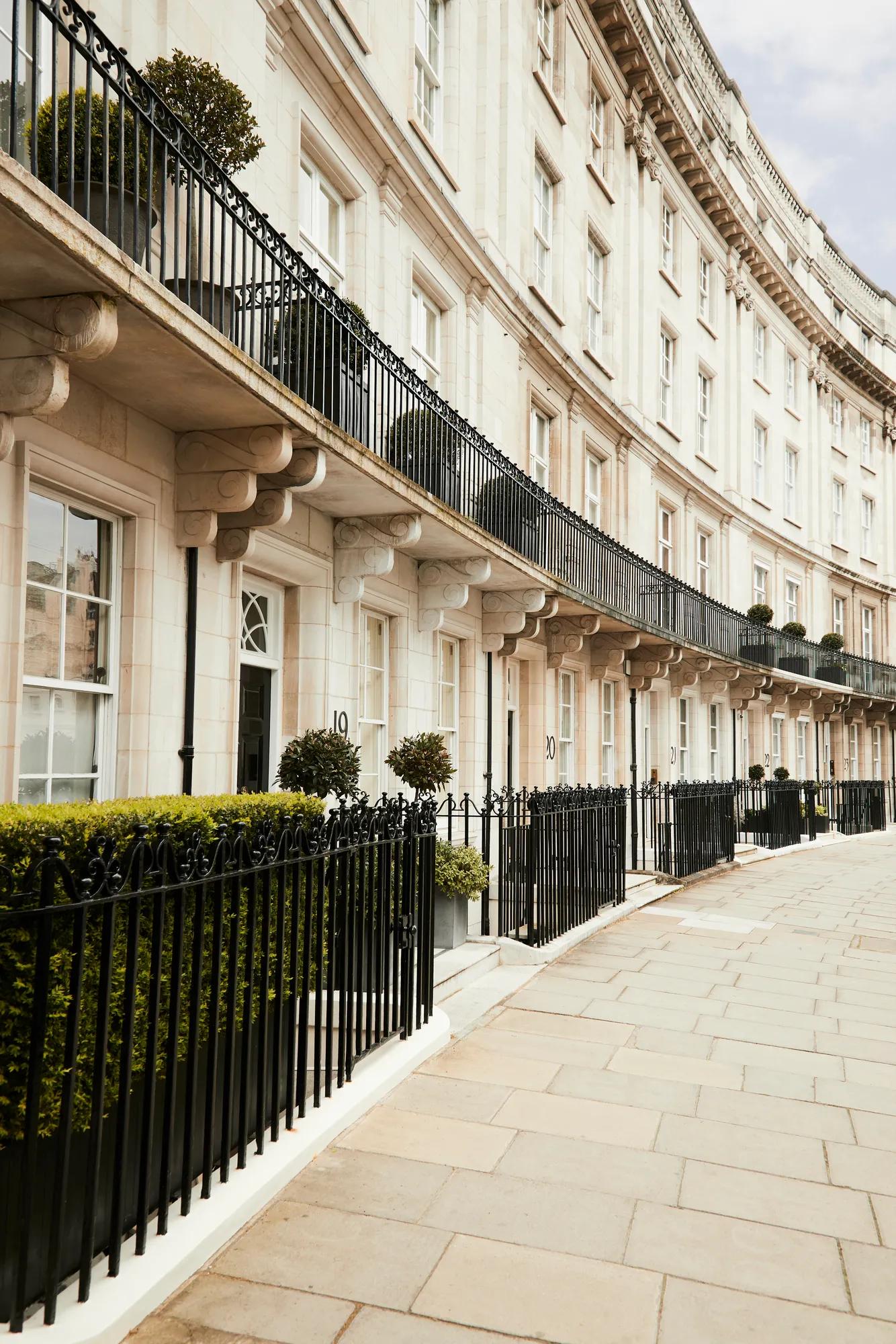 Elegant curved terrace of white stone houses with black railings, balconies, and potted greenery.