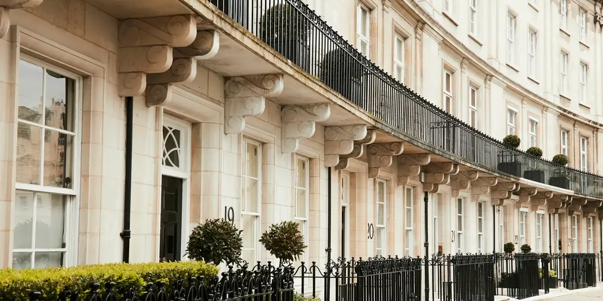 Elegant curved terrace of white stone houses with black railings, balconies, and potted greenery.