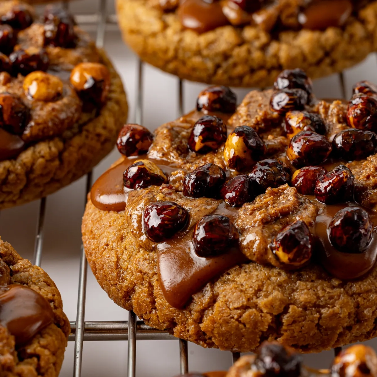 Close-up of caramel-topped cookies studded with glossy roasted nuts cooling on a wire rack.