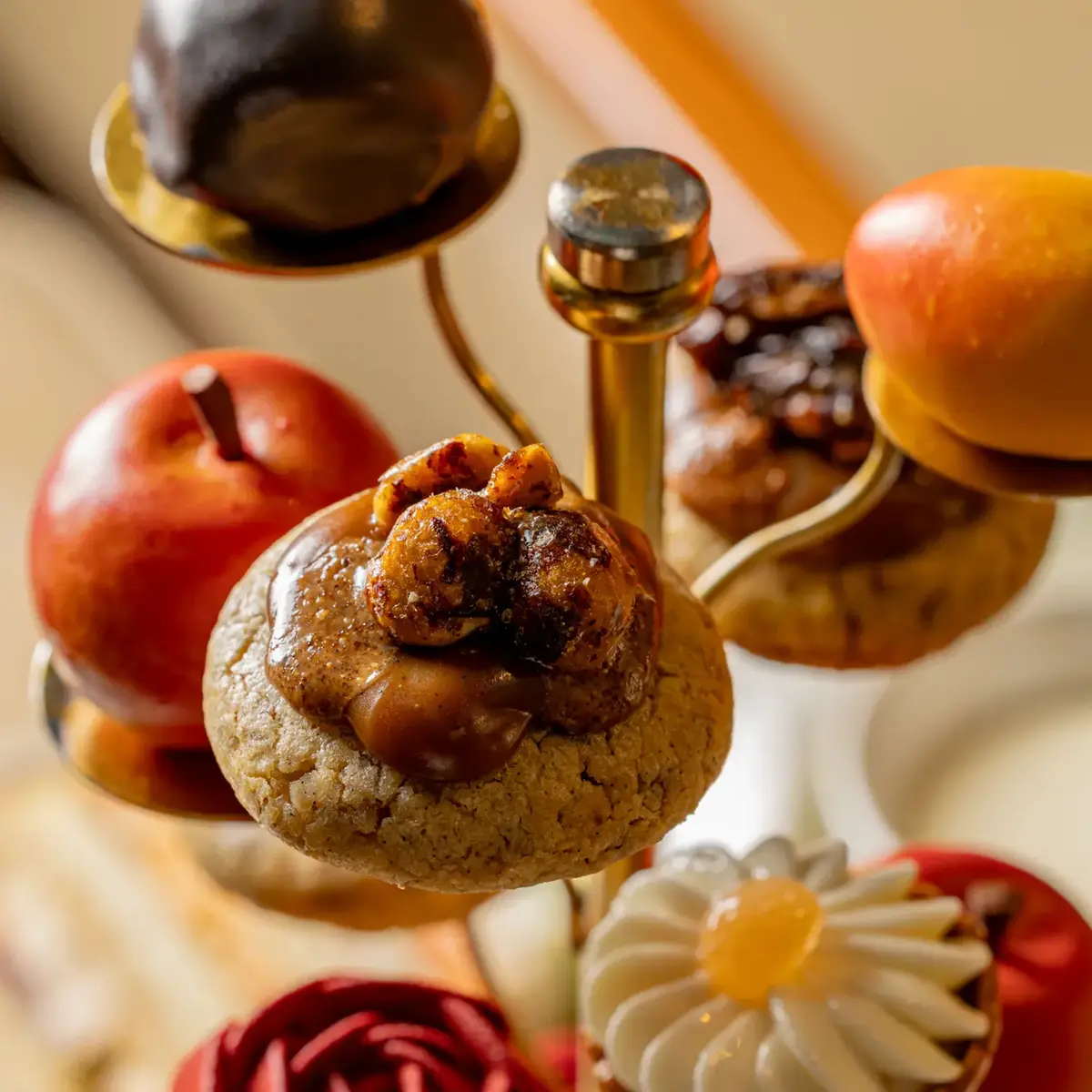 Close-up of a tiered stand with miniature pastries, including cookies, cream-topped tart and fruit, arranged on gold tiers.