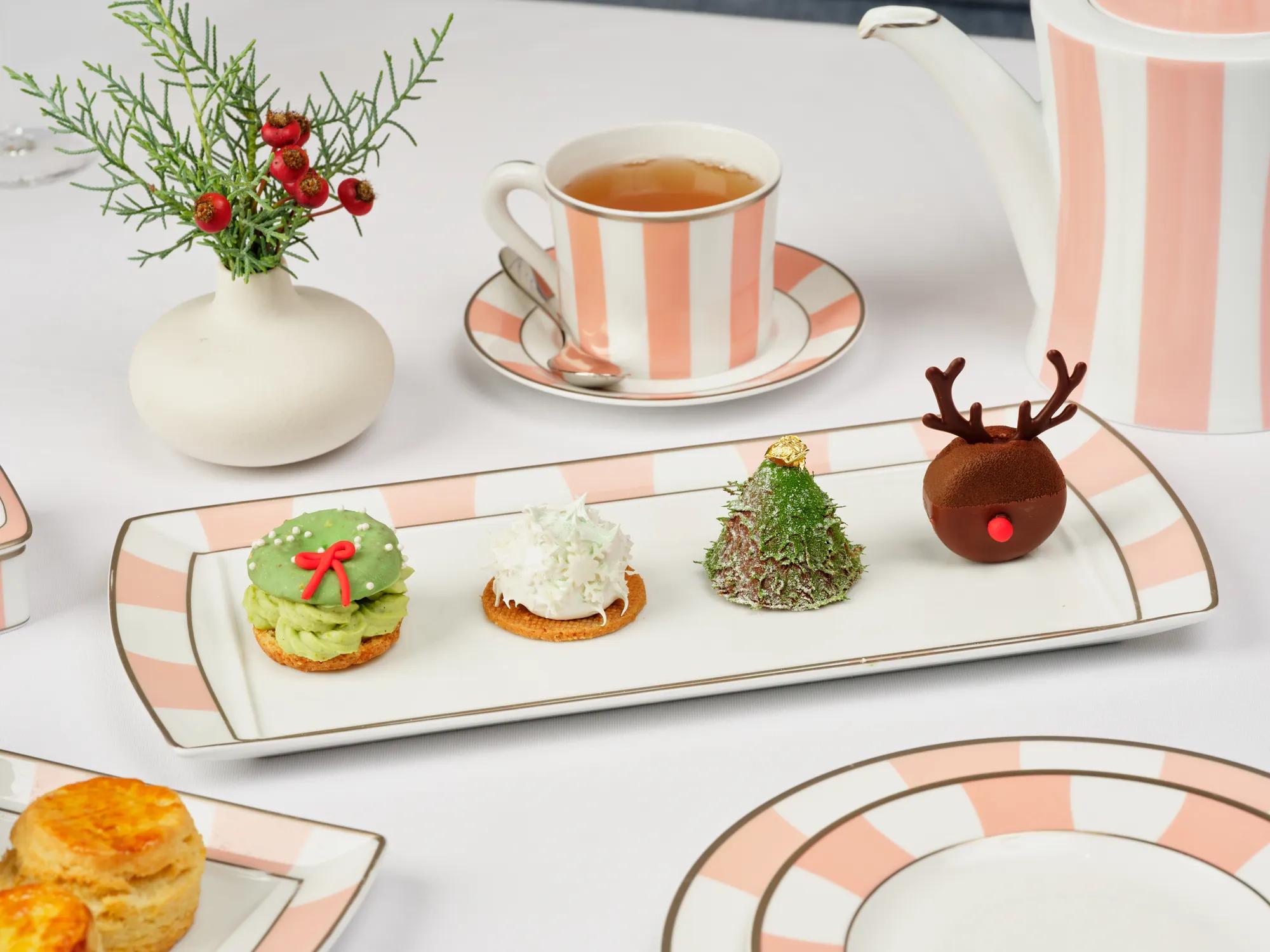 Festive afternoon tea featuring tea, Champagne, sandwiches, scones and holiday pastries, displayed beside elegant gift boxes.