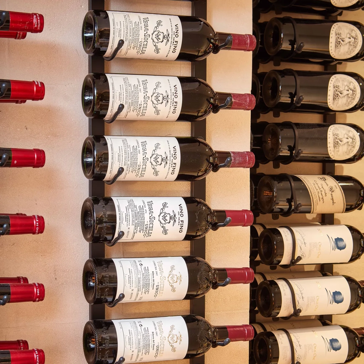 Wall-mounted wine racks holding rows of bottles with red and black caps displayed horizontally.