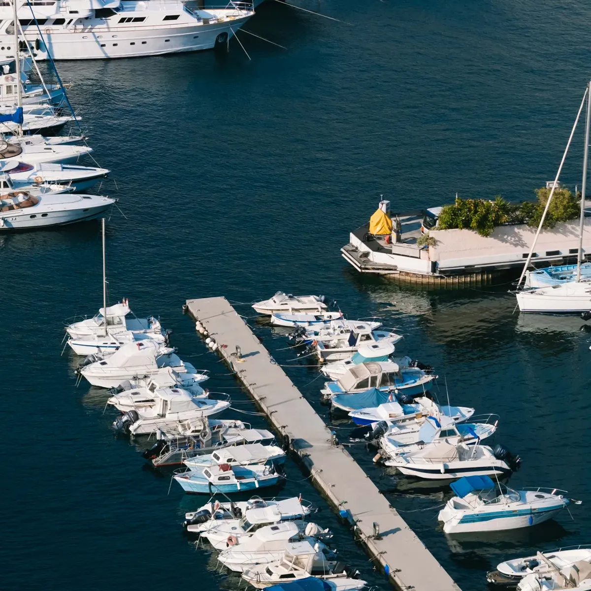 Aerial view of marina with luxury yachts, small boats moored along docks, and deep blue water.
