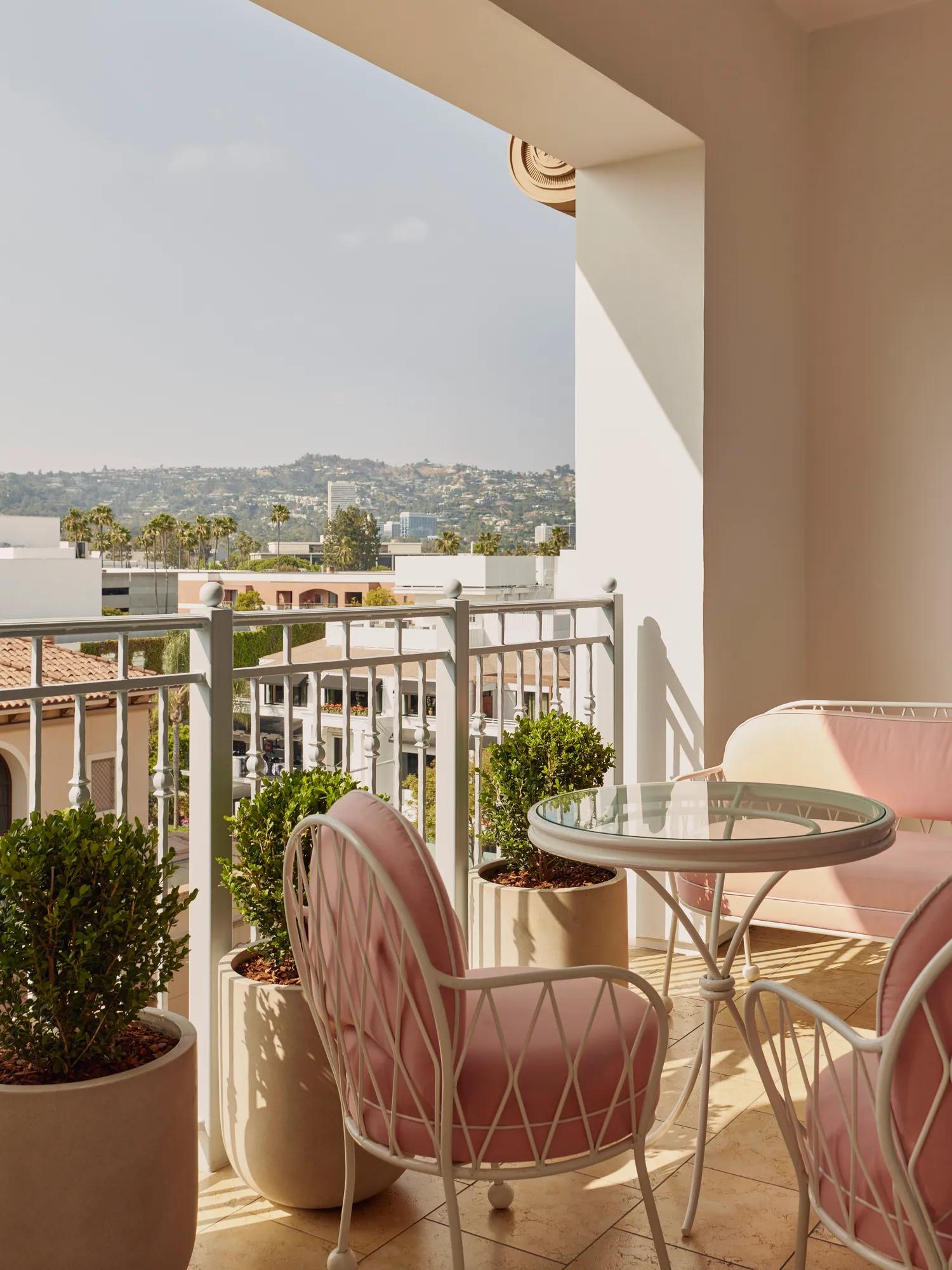 Covered terrace with pink cushioned chairs, glass‑top table, and planters overlooking Hollywood hills.