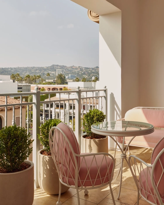 Covered terrace with pink cushioned chairs, glass‑top table, and planters overlooking Hollywood hills.