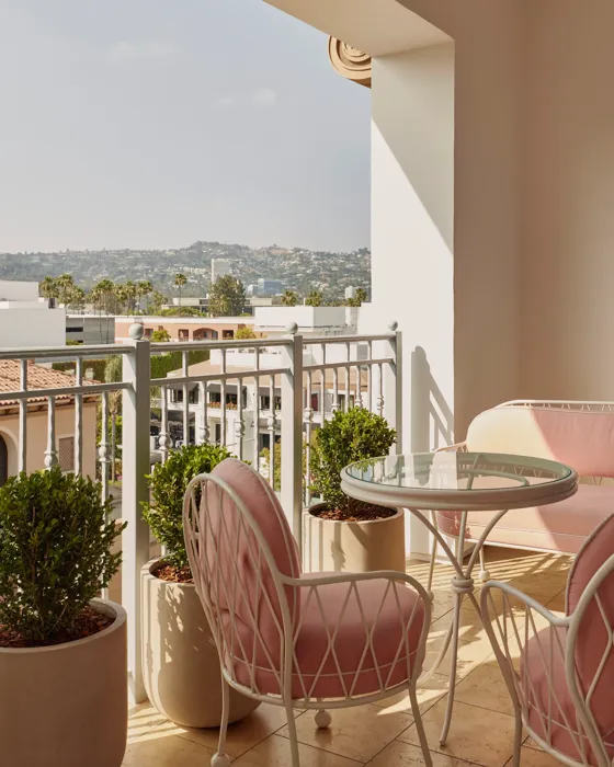 Covered terrace with pink cushioned chairs, glass‑top table, and planters overlooking Hollywood hills.