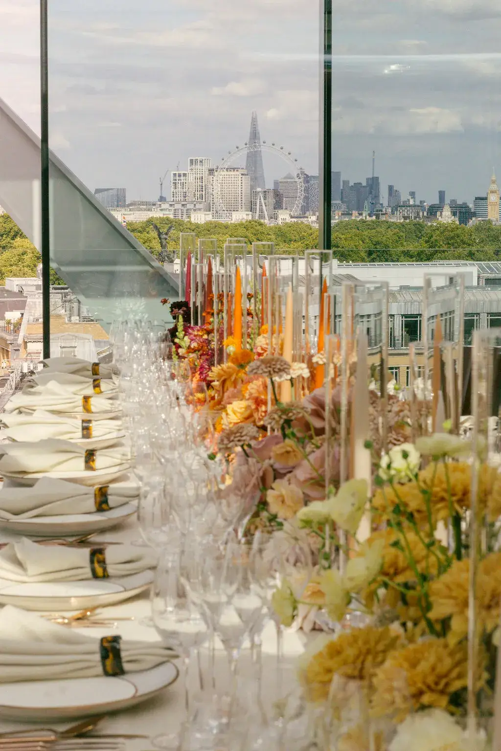 An elegant rooftop dining table with floral arrangements and glassware overlooking London’s skyline, including the Shard and London Eye.