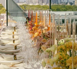 An elegant rooftop dining table with floral arrangements and glassware overlooking London’s skyline, including the Shard and London Eye.