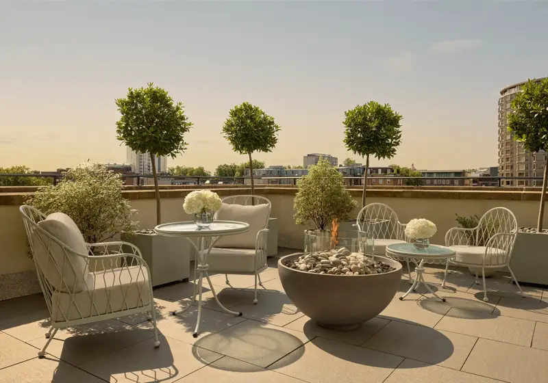 Rooftop terrace with cushioned seating, round tables, potted trees, and central fire pit overlooking city skyline.