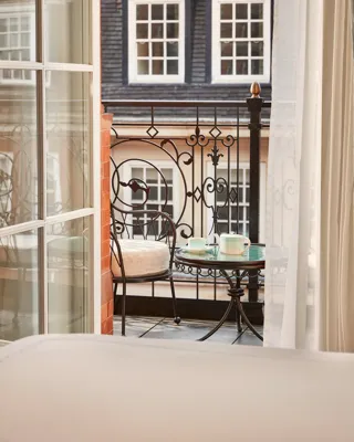 Intimate balcony with wrought-iron railing, a small round table set with teacups, and two cushioned chairs overlooking classic townhouse windows.