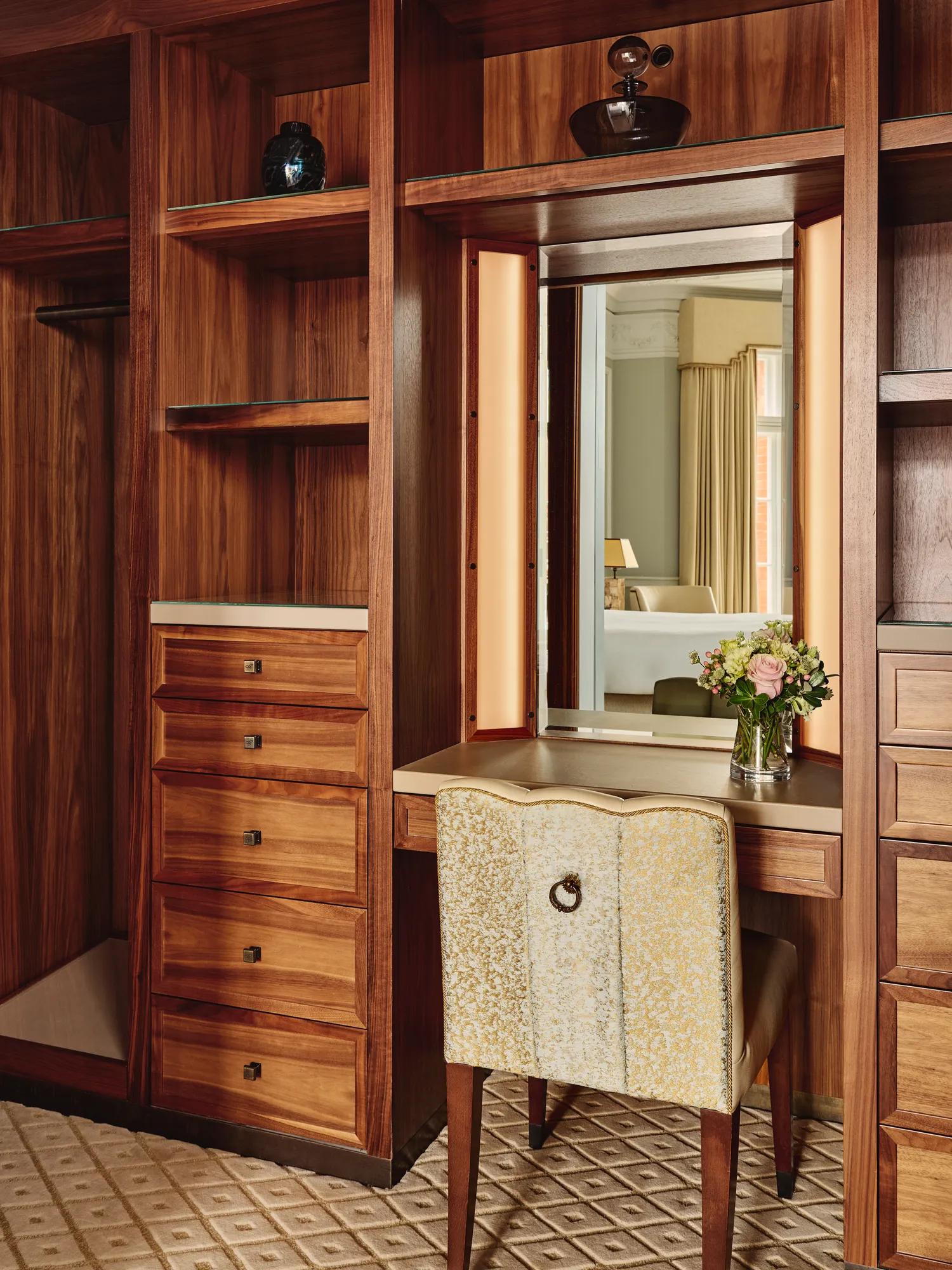 Wood-paneled dressing area with vanity mirror, upholstered chair, drawers, and shelving.