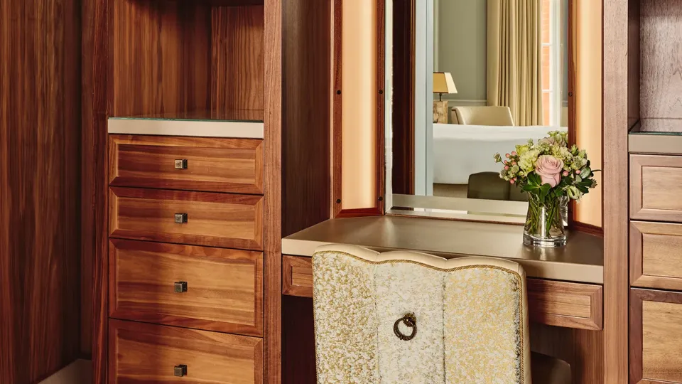 Wood-paneled dressing area with vanity mirror, upholstered chair, drawers, and shelving.