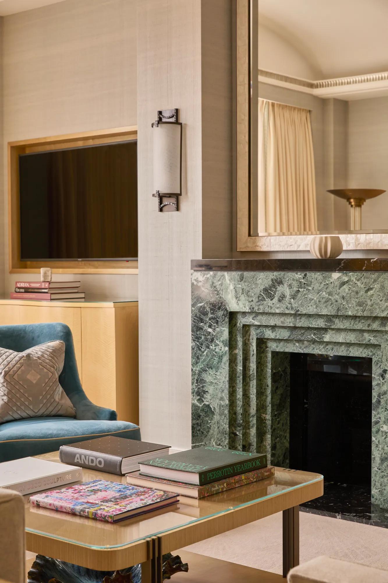 Detail of a contemporary living room featuring a green marble fireplace, coffee table with books, blue armchair and wall-mounted television.