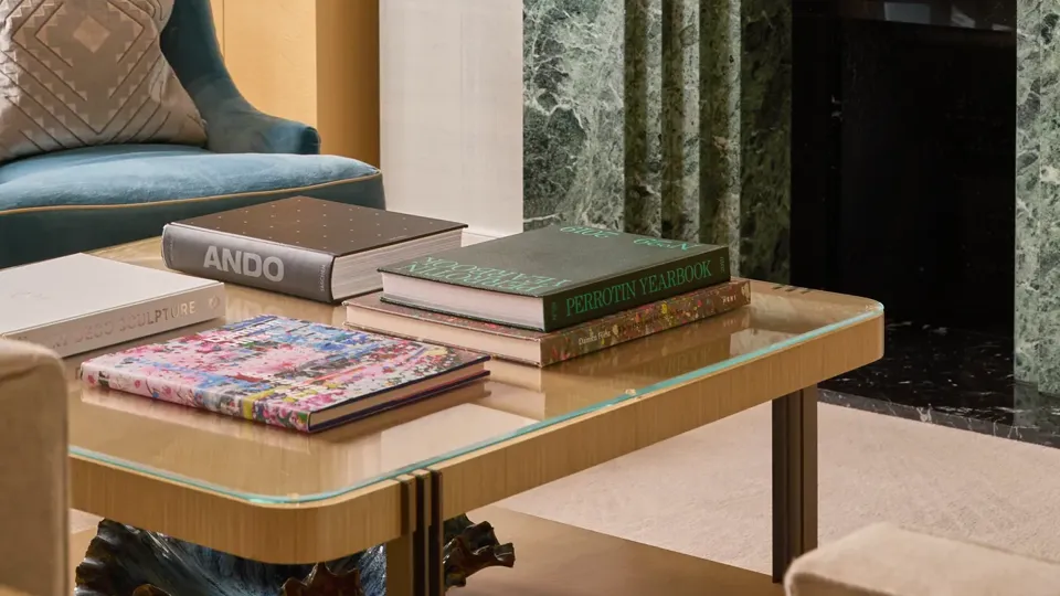 Detail of a contemporary living room featuring a green marble fireplace, coffee table with books, blue armchair and wall-mounted television.
