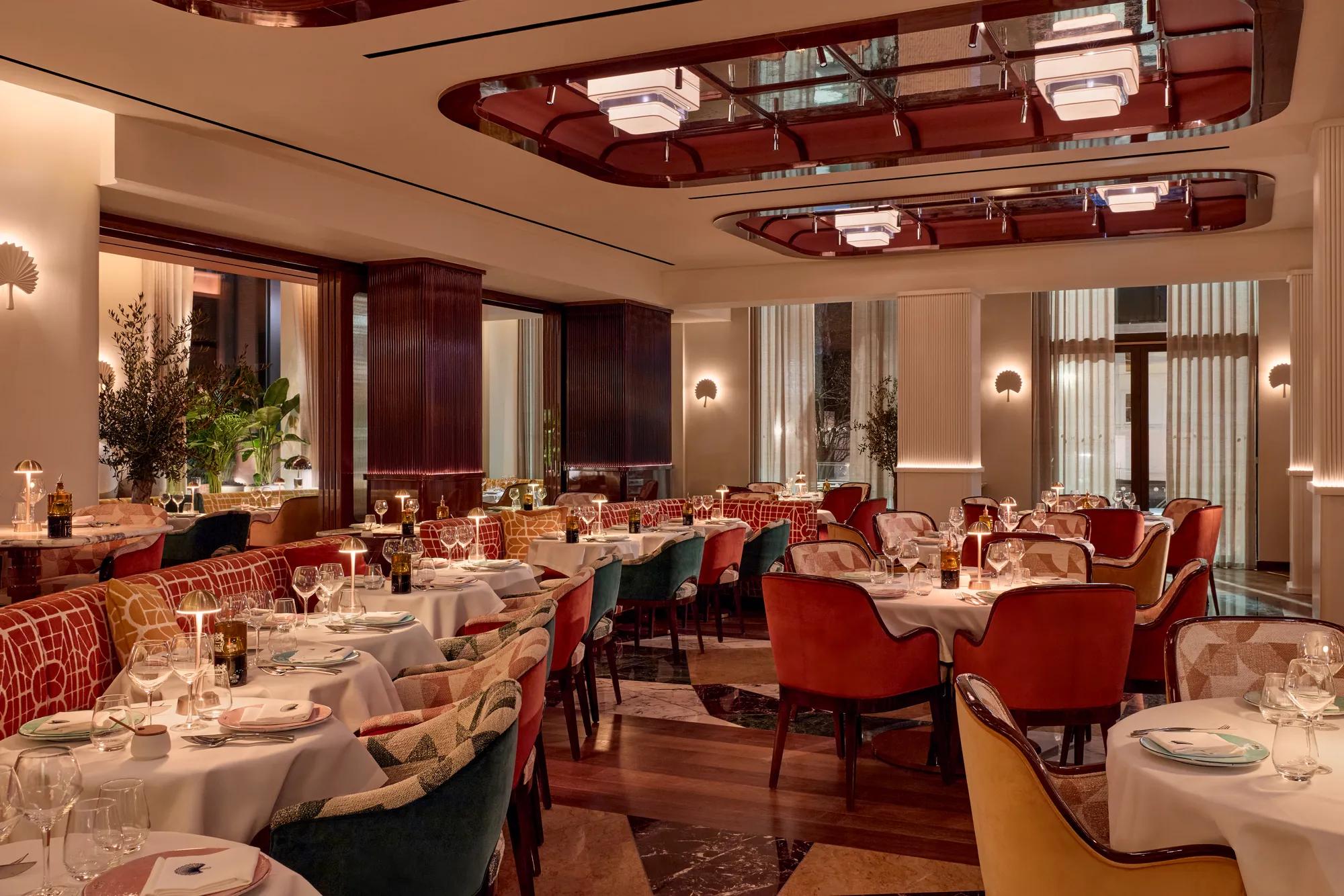 Elegant dining room at La Môme London, featuring plush seating, marble-topped tables and warm, ambient lighting.