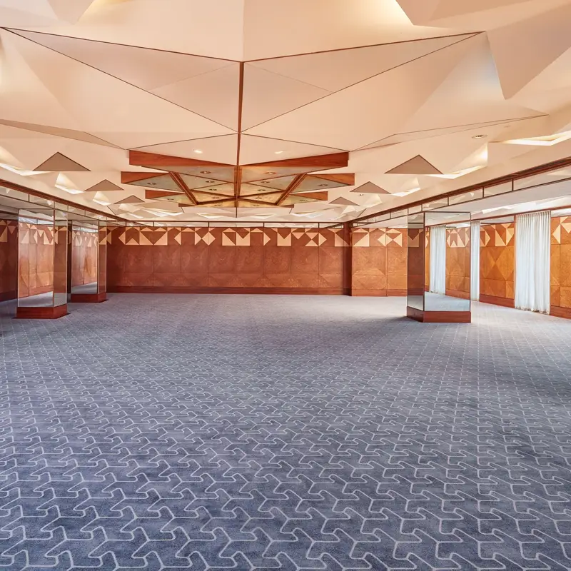Spacious hotel ballroom with geometric ceiling design, patterned carpet, and mirrored walls for events