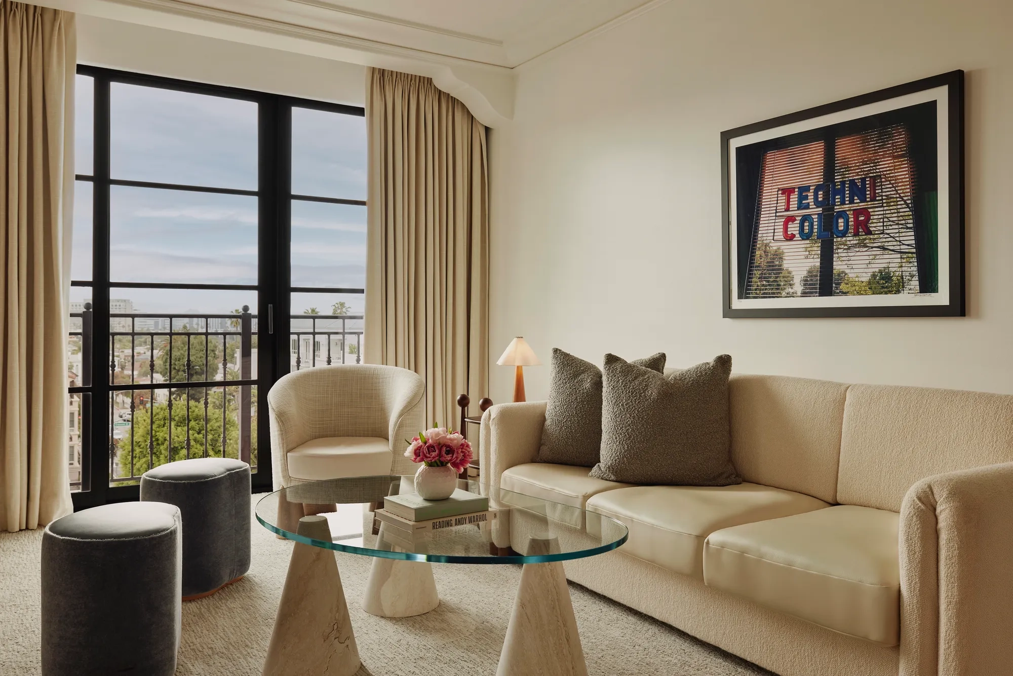 Living room in Maybourne Beverly Hills Library Suite with sofa, armchairs, glass table, and balcony view.