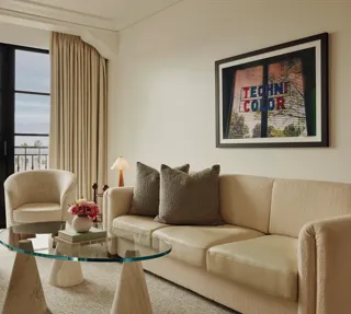Living room in Maybourne Beverly Hills Library Suite with sofa, armchairs, glass table, and balcony view.