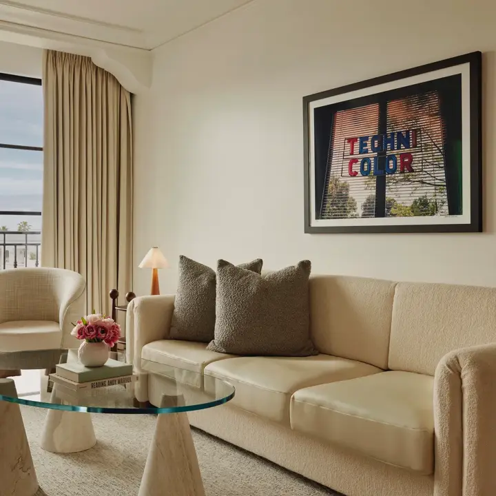 Living room in Maybourne Beverly Hills Library Suite with sofa, armchairs, glass table, and balcony view.
