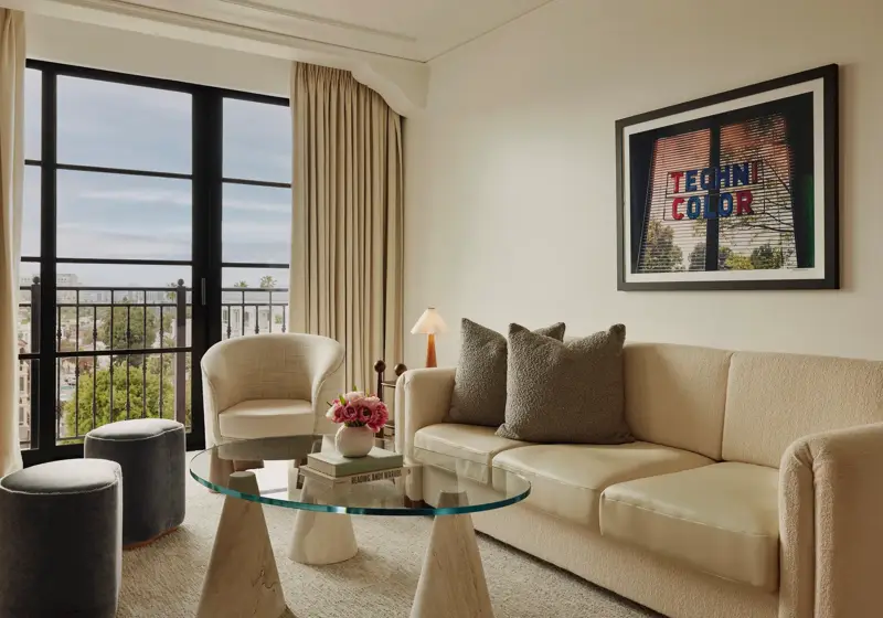 Living room in Maybourne Beverly Hills Library Suite with sofa, armchairs, glass table, and balcony view.