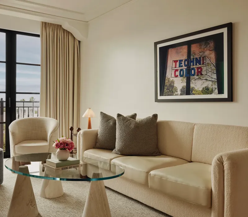 Living room in Maybourne Beverly Hills Library Suite with sofa, armchairs, glass table, and balcony view.