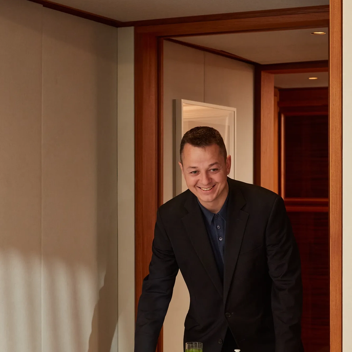 Smiling server presenting table with croissants, fresh fruit, juices, jams, and tea in hotel suite.