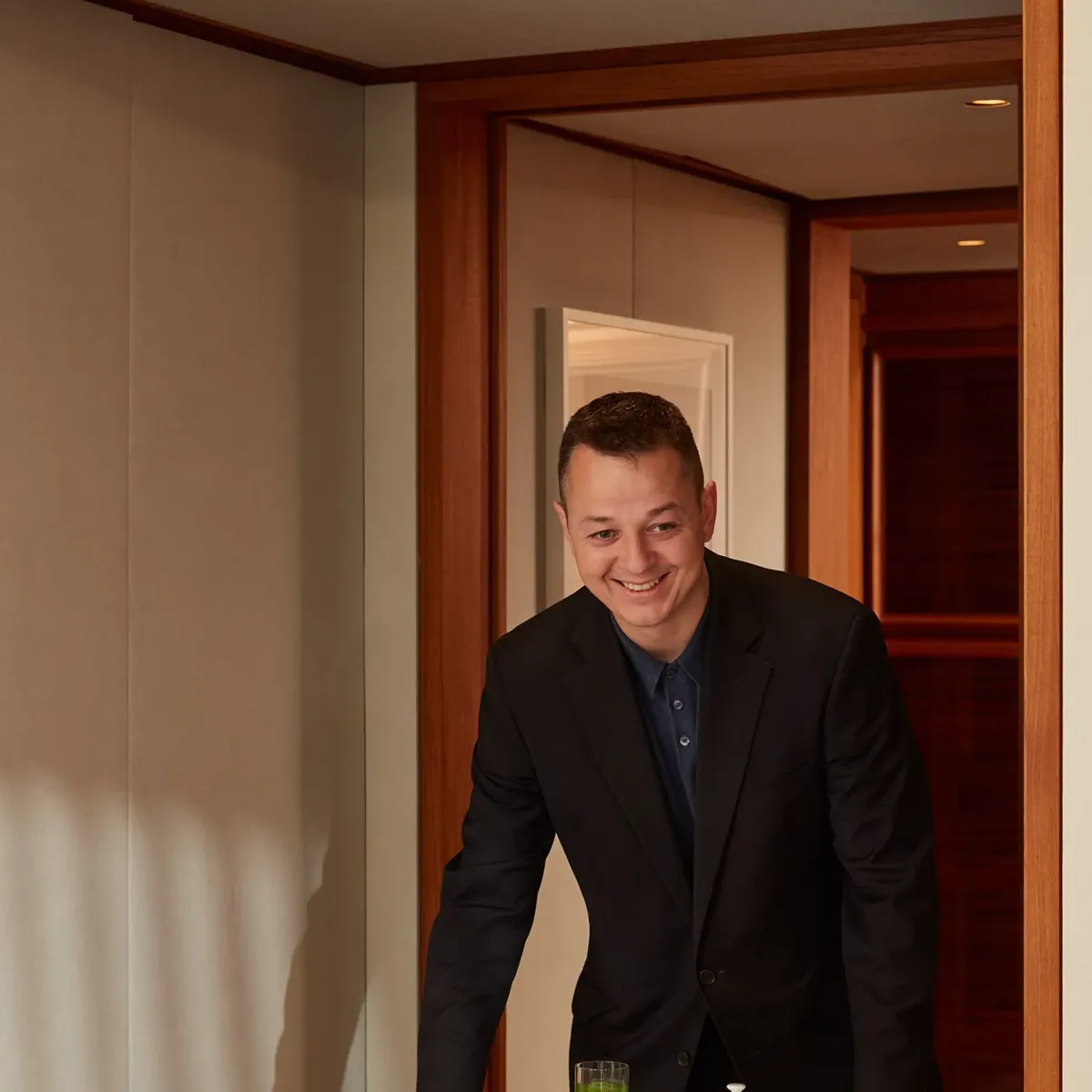 Smiling server presenting table with croissants, fresh fruit, juices, jams, and tea in hotel suite.