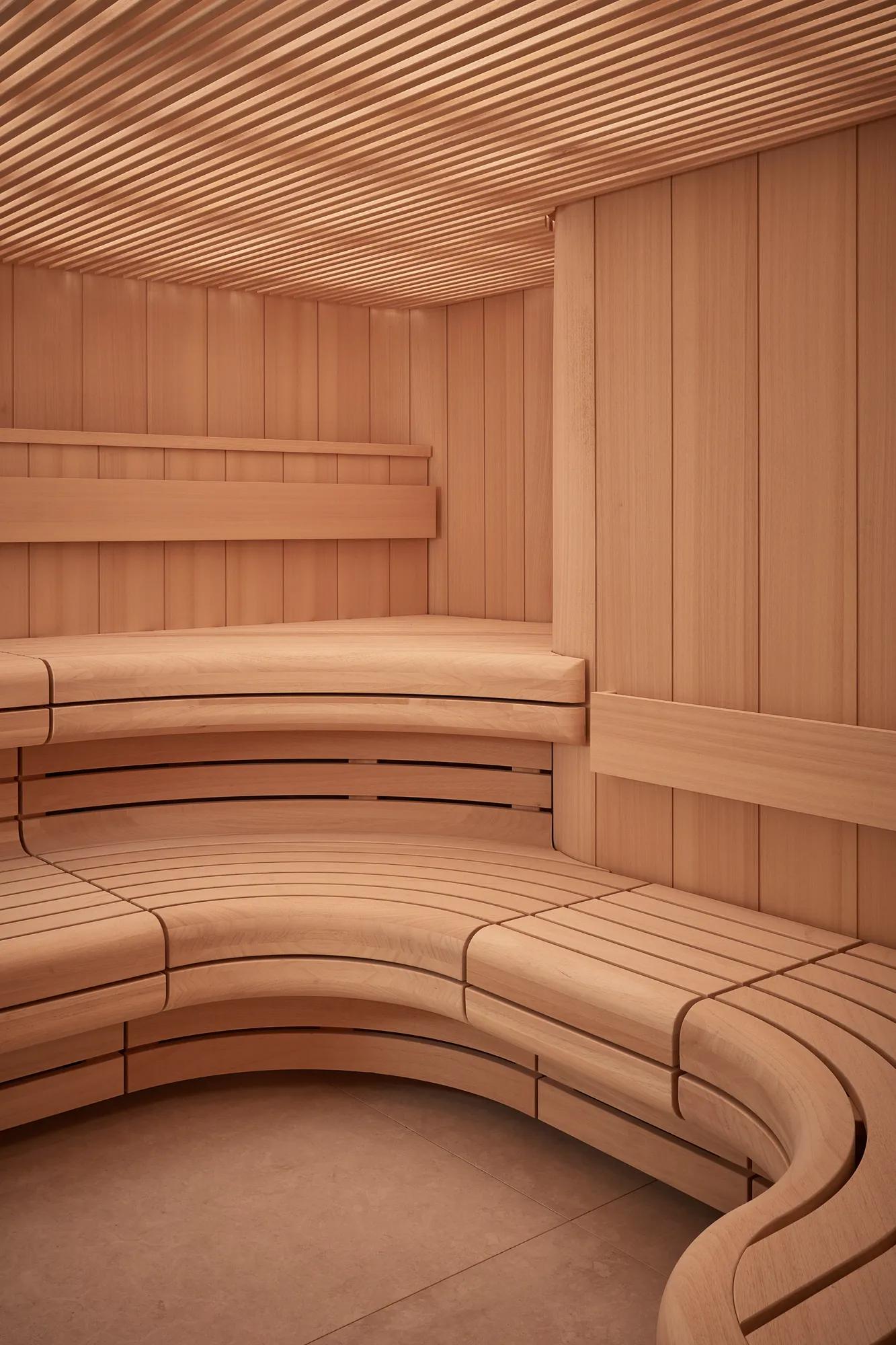 Curved wooden sauna interior with tiered bench seating and slatted walls and ceiling.