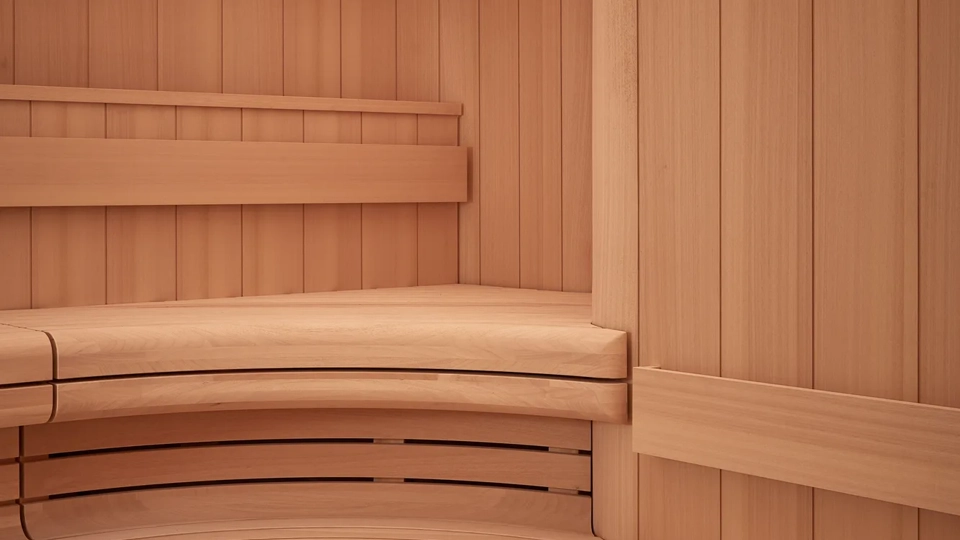 Curved wooden sauna interior with tiered bench seating and slatted walls and ceiling.