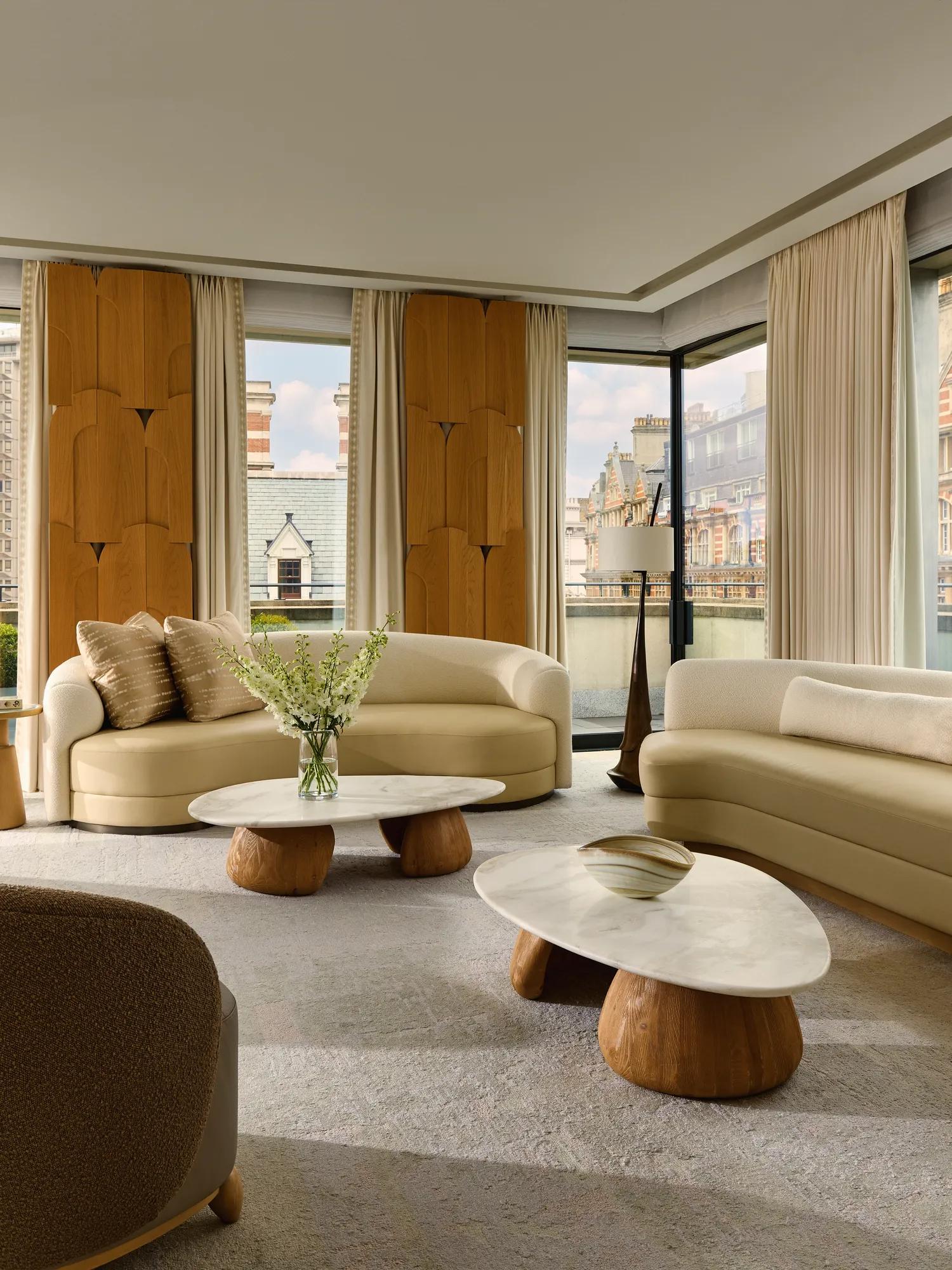 Bright penthouse living room with curved sofas, marble tables, and city views through floor-to-ceiling windows