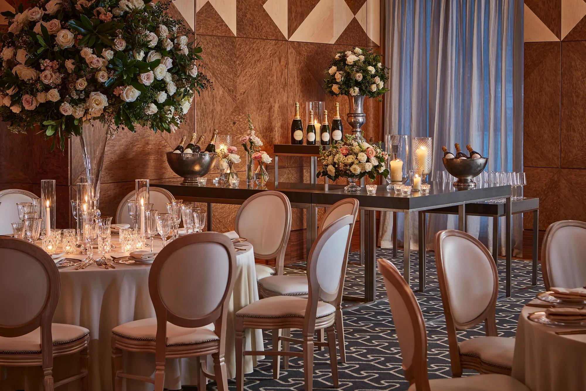 Elegant tables set with flowers, candles, and champagne bottles in a warmly lit wood-panelled ballroom.