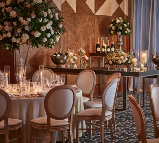 Elegant tables set with flowers, candles, and champagne bottles in a warmly lit wood-panelled ballroom.