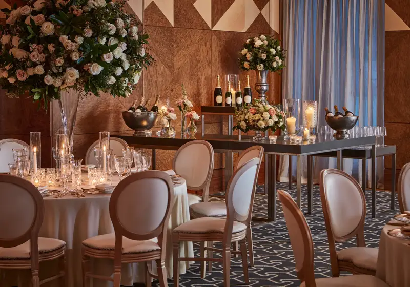 Elegant tables set with flowers, candles, and champagne bottles in a warmly lit wood-panelled ballroom.