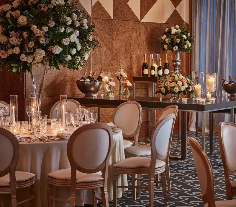 Elegant tables set with flowers, candles, and champagne bottles in a warmly lit wood-panelled ballroom.