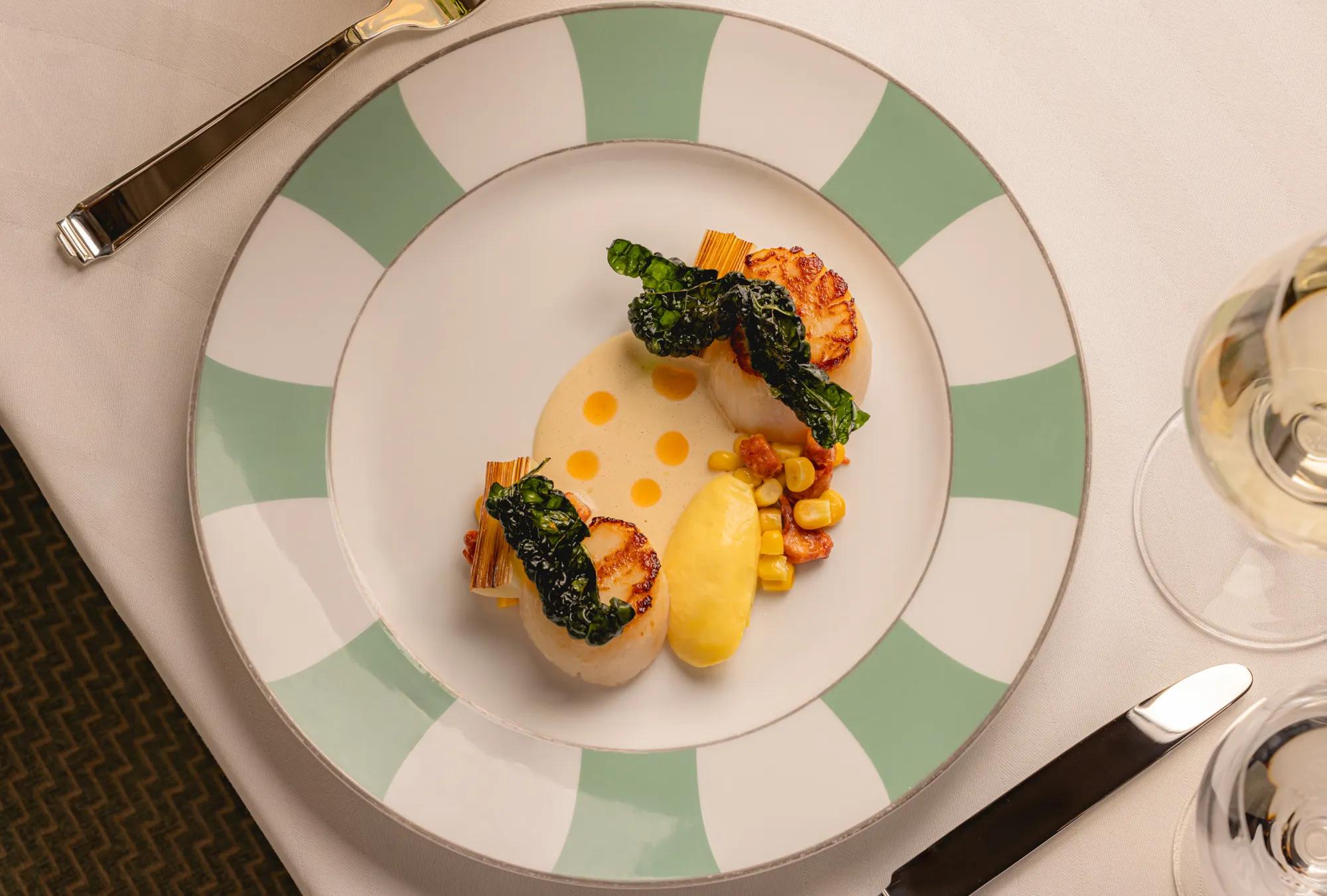 Seared scallops with charred baby leeks, sweetcorn, cavolo nero, and a quenelle of purée.