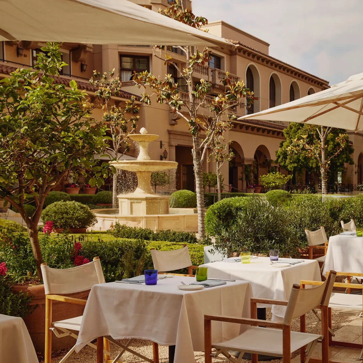 The Terrace outdoor dining beside a tiered stone fountain, white umbrellas and manicured garden.
