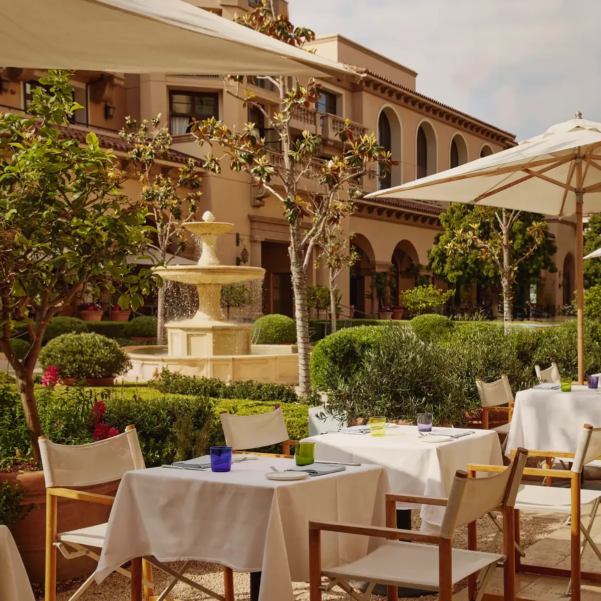 The Terrace outdoor dining beside a tiered stone fountain, white umbrellas and manicured garden.