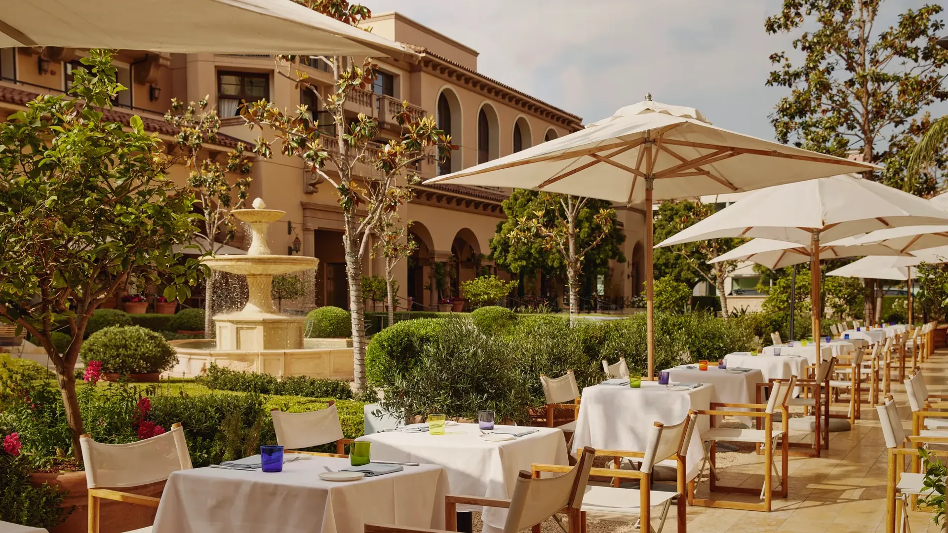 The Terrace outdoor dining beside a tiered stone fountain, white umbrellas and manicured garden.