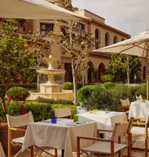 The Terrace outdoor dining beside a tiered stone fountain, white umbrellas and manicured garden.