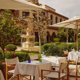 The Terrace outdoor dining beside a tiered stone fountain, white umbrellas and manicured garden.