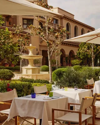 The Terrace outdoor dining beside a tiered stone fountain, white umbrellas and manicured garden.